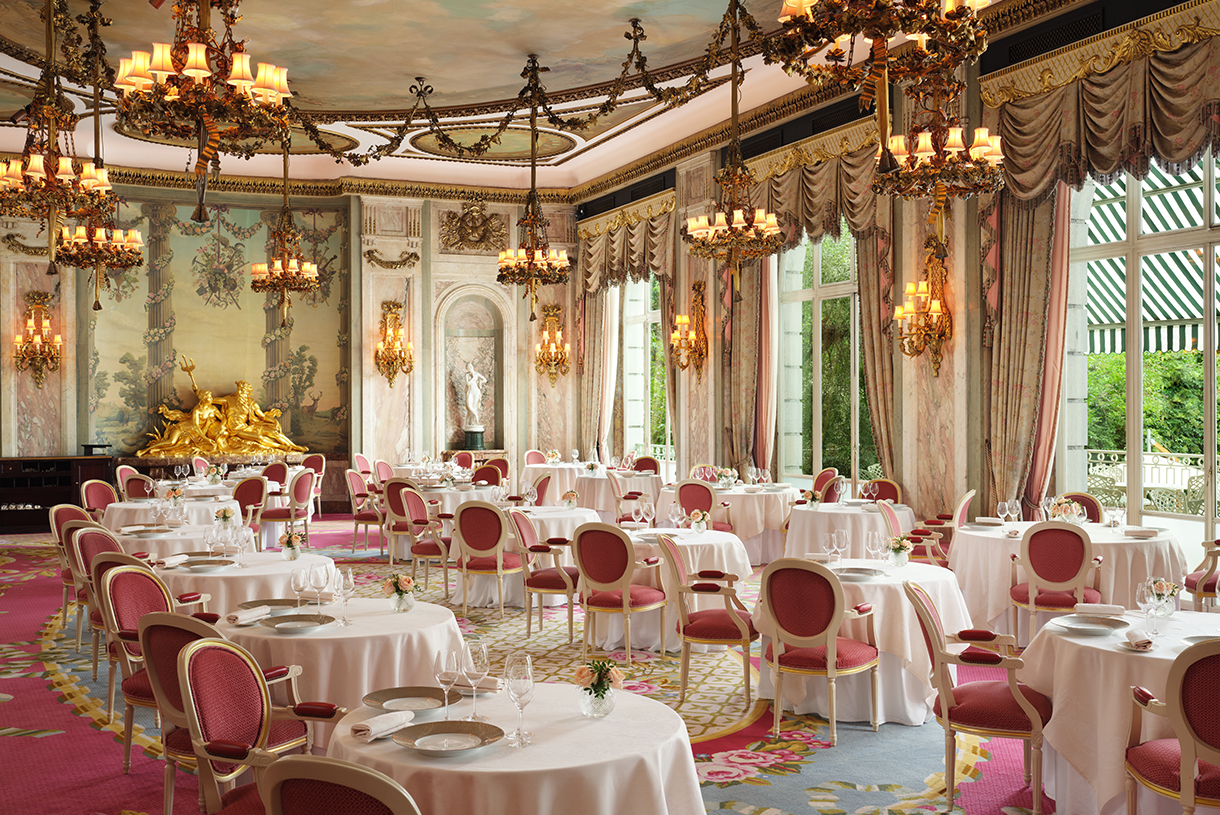 Interior of elegant and grand dining room at the Ritz London. The Ritz Restaurant is decorated with chandeliers, statues, paintings, and windows overlooking the park outside.